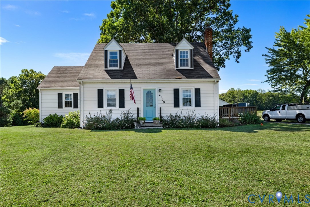 White exterior with black shutters, dormer windows, a light blue front door, and a side deck