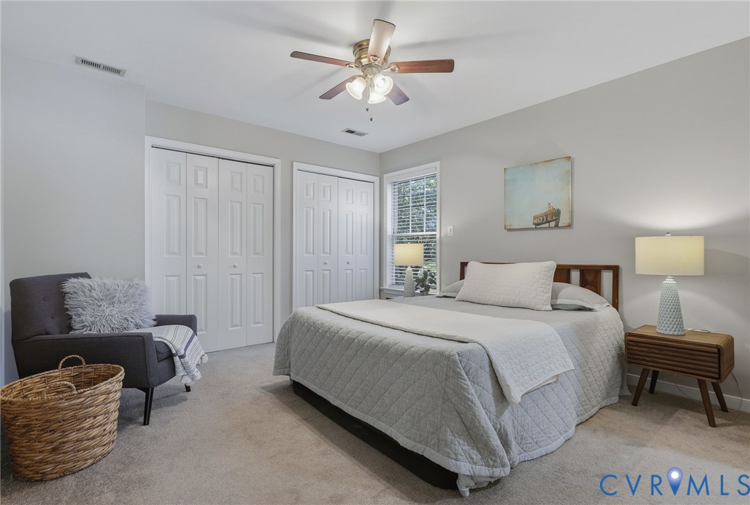 Soft gray wall tones, ceiling fan with integrated lighting, wood headboard, two white bi-fold closet doors, and natural light from a window with blinds