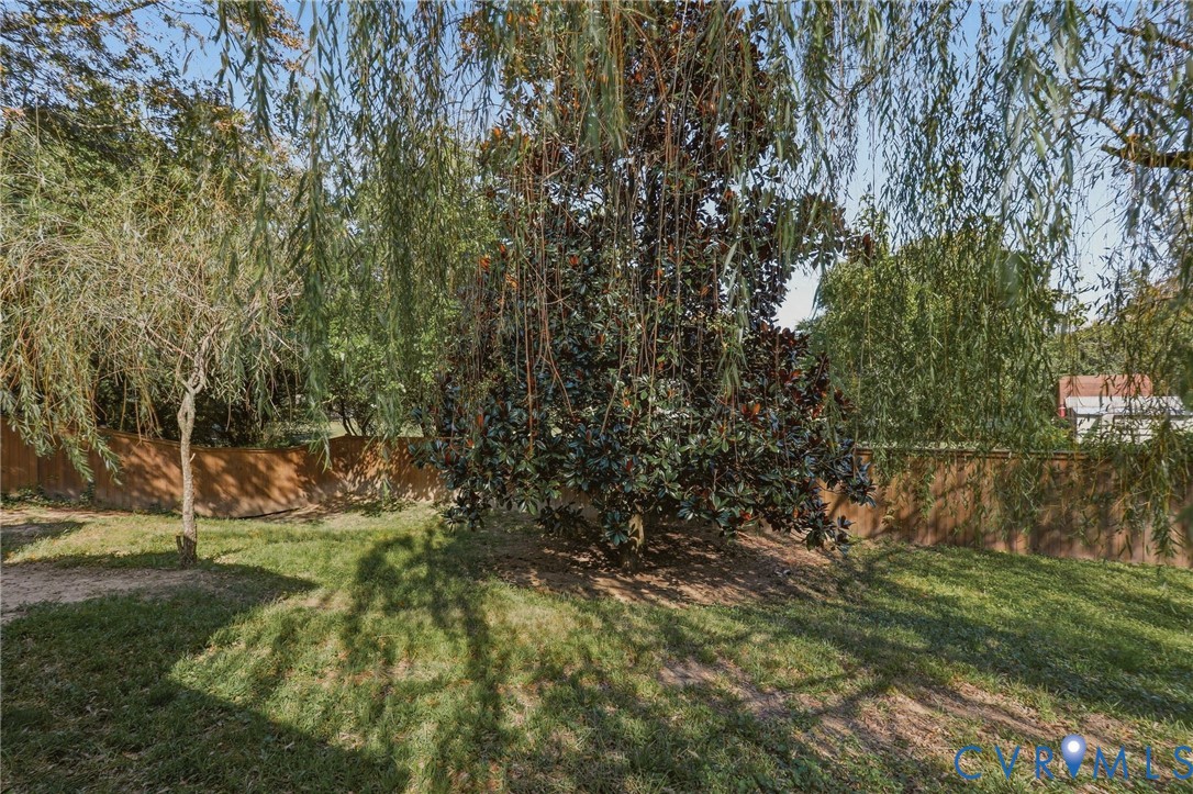 Expansive grassy area featuring mature trees and a privacy fence