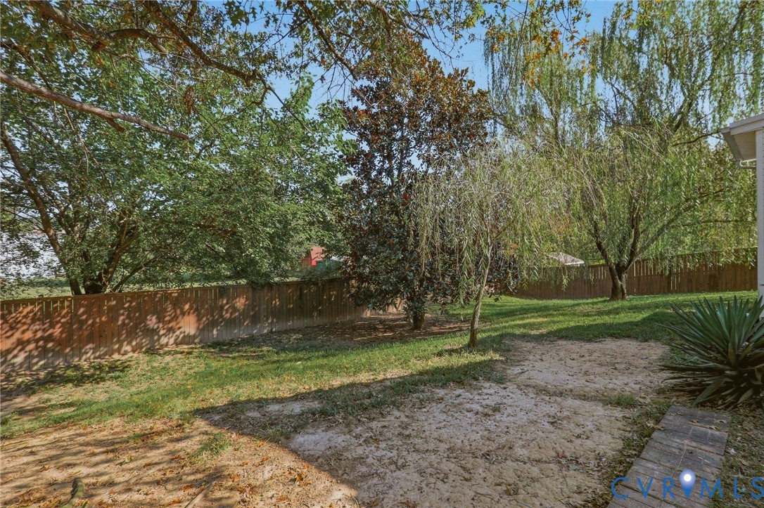 Expansive backyard featuring a wood fence, mature trees, and a brick paver pathway