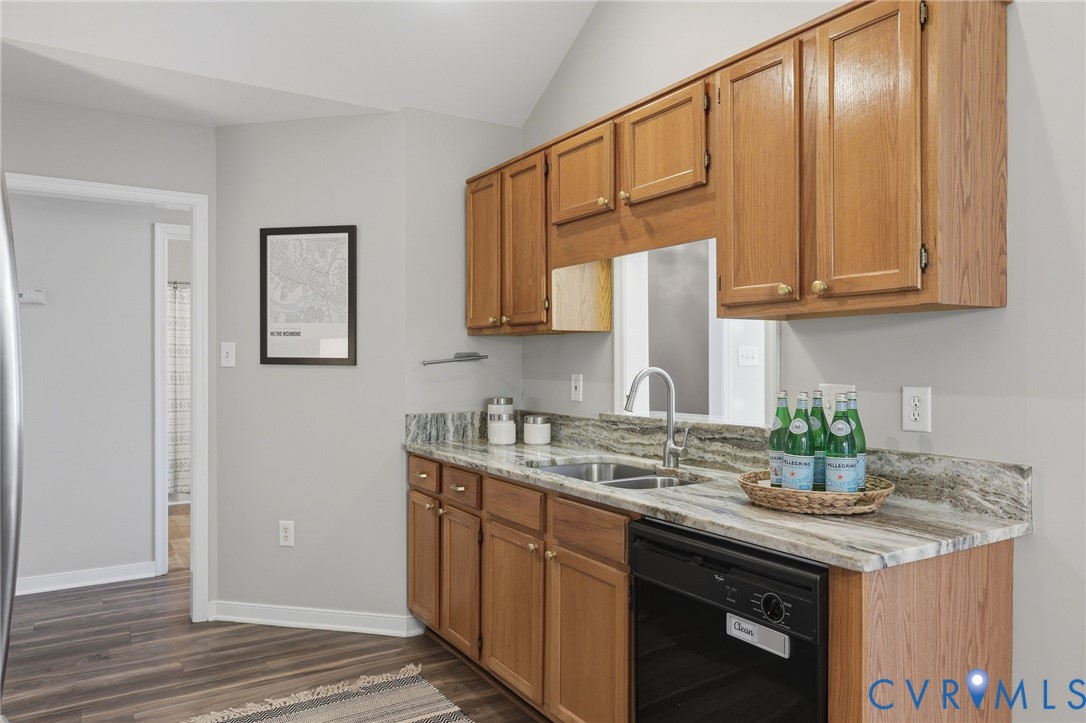 Kitchen featuring wood cabinetry, a stainless steel sink, a black dishwasher, and stone countertops