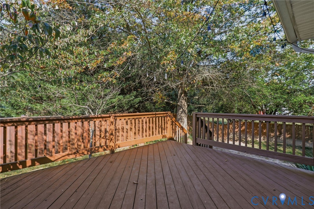 Expansive wood deck with a perimeter railing and integrated steps, surrounded by mature trees