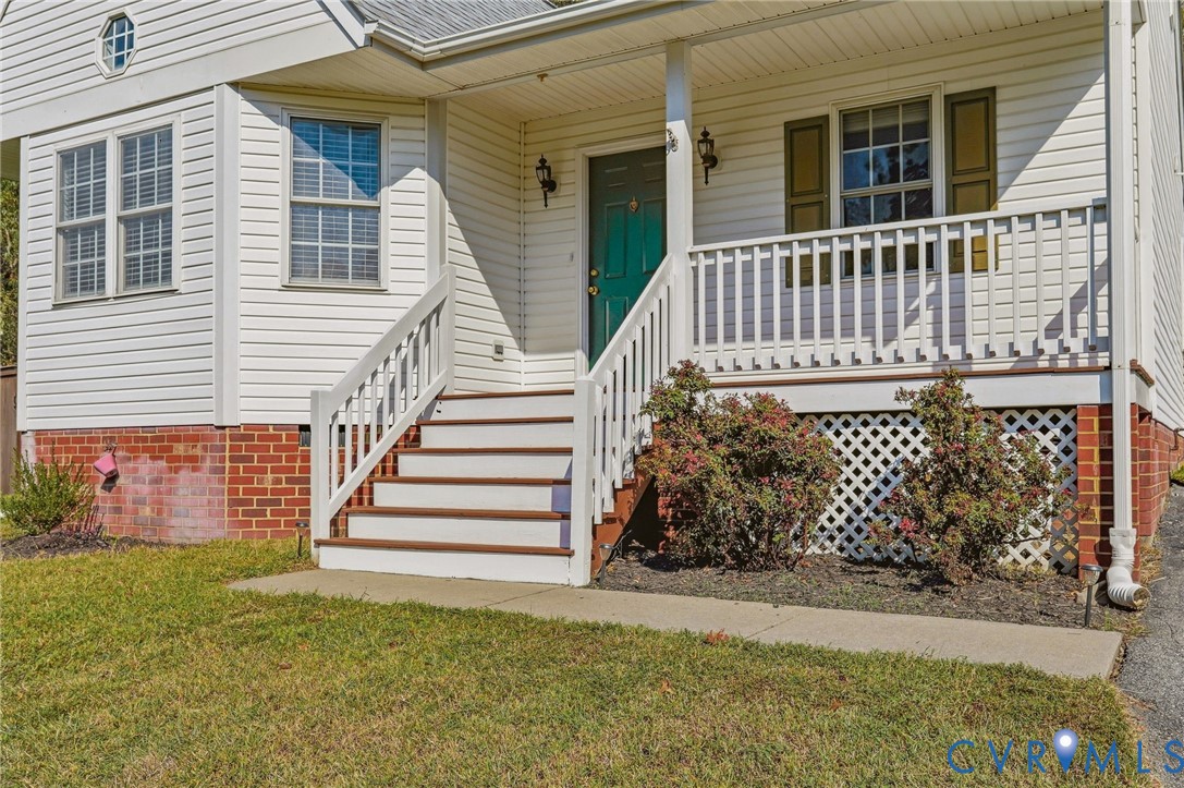 Front exterior featuring white siding, a brick foundation, a covered porch with white railings, and a vibrant green front door Front exterior featuring white siding, a brick foundation, a covered porch with white railings, and a vibrant green front door