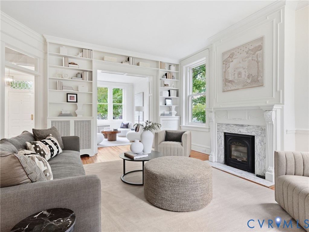 Hardwood flooring throughout, built-in shelving, marble-clad fireplace, detailed crown molding, and large windows