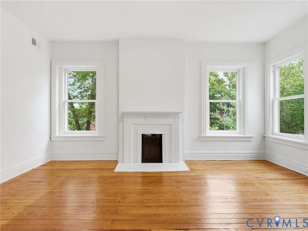 Hardwood flooring, three sash windows, white trim, and a decorative fireplace