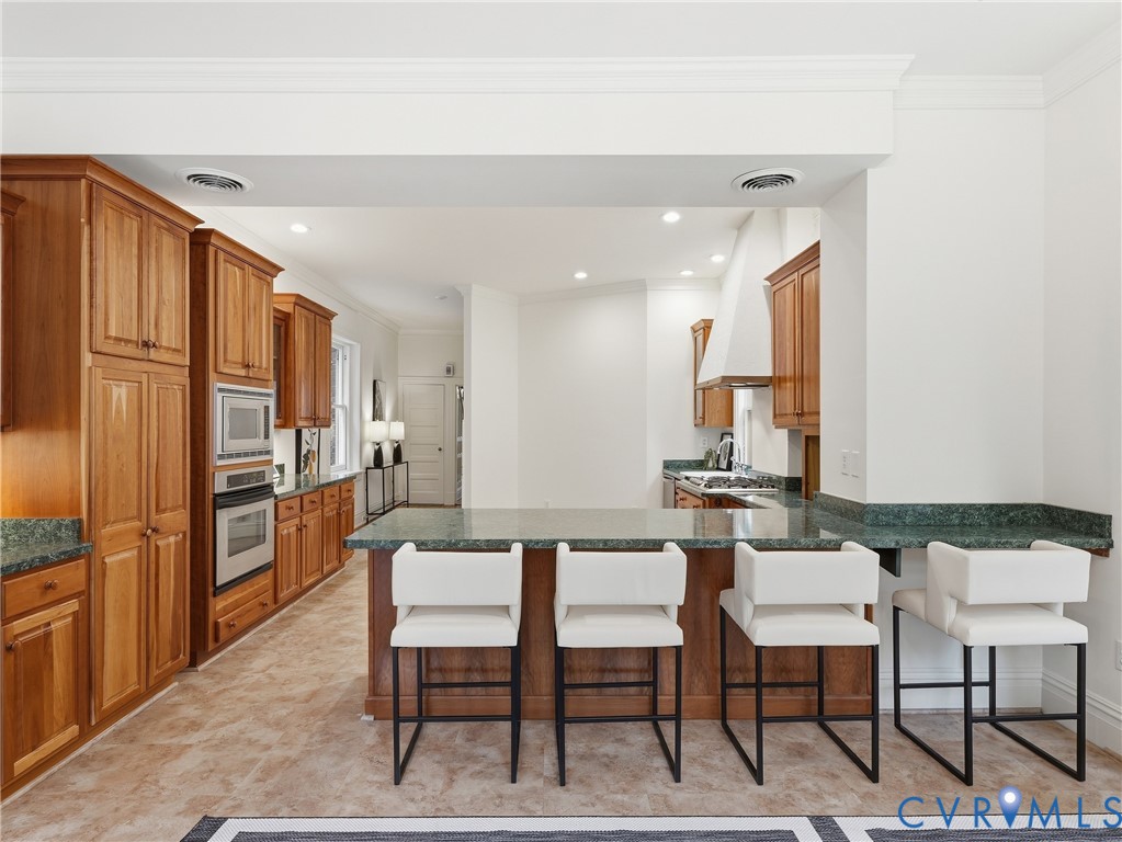 Expansive kitchen featuring wood cabinetry, integrated stainless steel appliances, a generous island with seating, and a matching stone countertop
