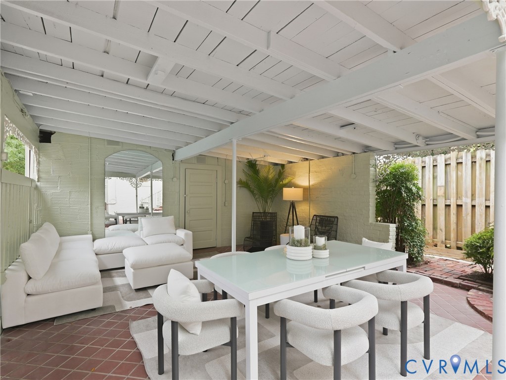 Covered outdoor patio with exposed beam ceiling, brick paver flooring, and privacy fencing