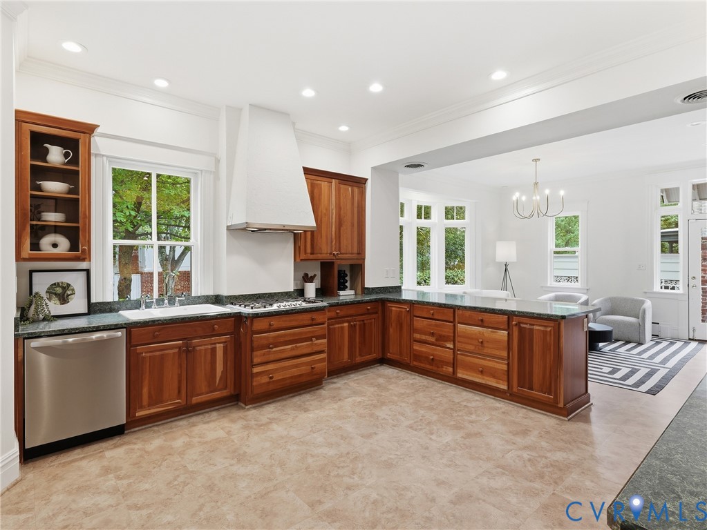 Kitchen featuring wood cabinetry, dark countertops, a stainless steel dishwasher, and a white range hood