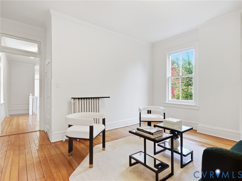 Hardwood flooring throughout, white painted walls, crown molding, and a window with white trim