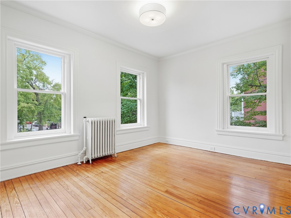 Light wood-finish flooring, three windows with white trim, white walls, and a ceiling-mounted light fixture