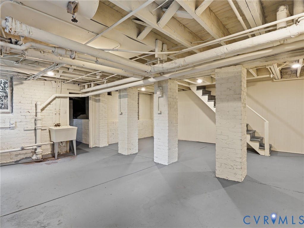 Painted brick walls, exposed ceiling joists, concrete flooring, utility sink, and staircase