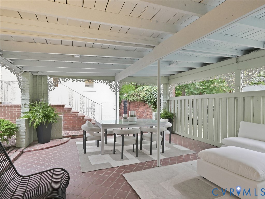 Covered patio featuring red tile flooring, exposed beam ceiling, brickwork, and a slatted privacy fence