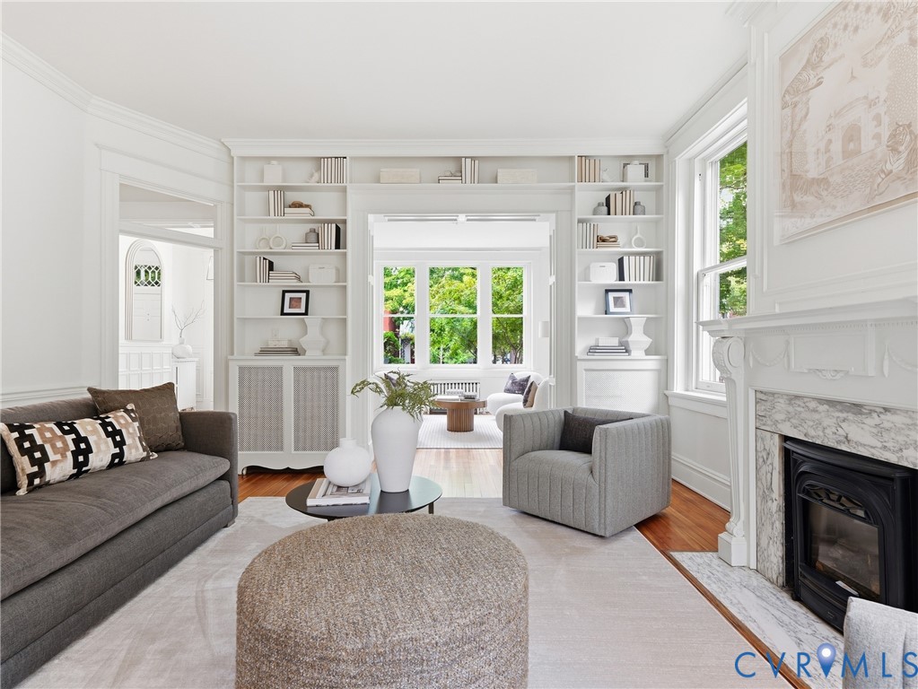 Hardwood flooring, built-in shelving, decorative fireplace with a stone surround, white trim, and crown molding