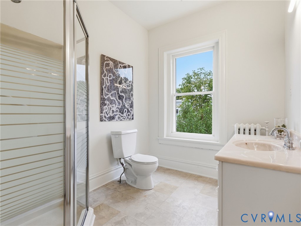 Shower enclosure with frosted glass, white vanity with integrated sink, chrome faucet, window with white trim, and tile flooring