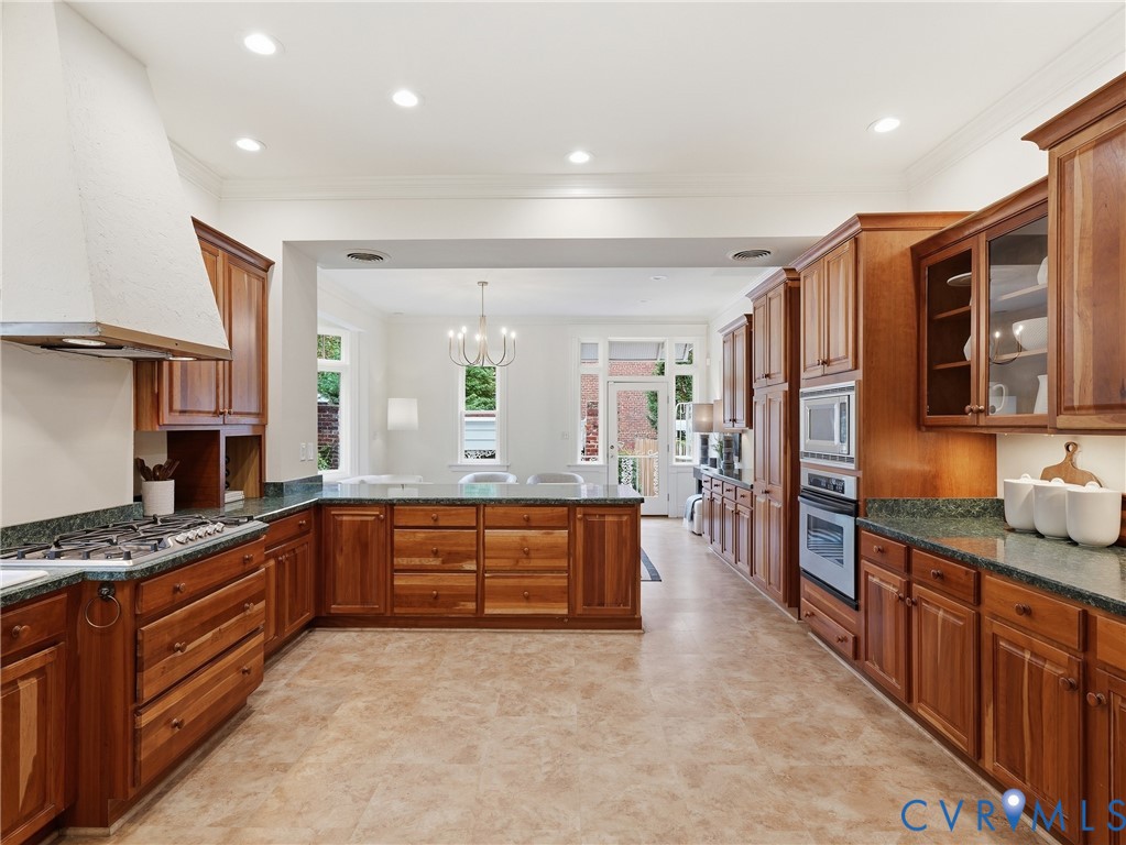 Expansive kitchen featuring wood cabinetry, integrated stainless steel appliances, a gas cooktop with a range hood, and resilient flooring