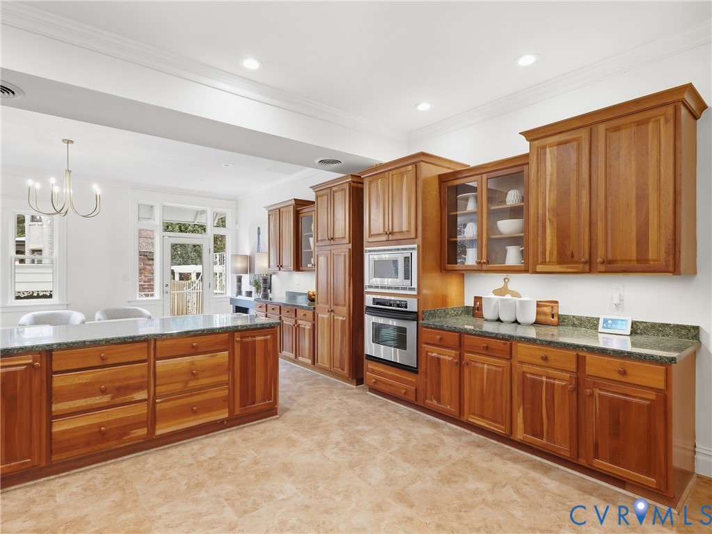 Wood-finish cabinetry with glass-front accents, stainless steel built-in appliances, stone countertops, and recessed lighting