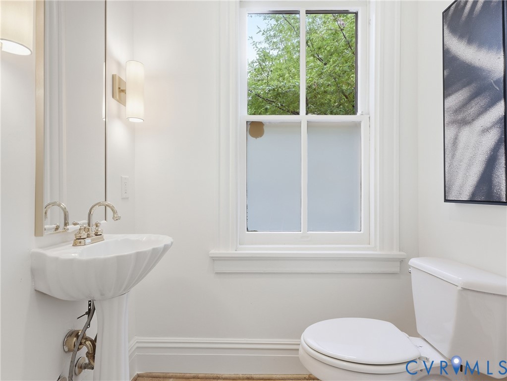 Pedestal sink with polished nickel faucet, wall-mounted sconce lighting, and a white framed window