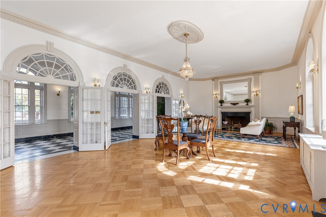 Parquet hardwood flooring, arched glass-paneled double doors with transom windows, crown molding, fireplace with mantel, and a decorative ceiling medallion