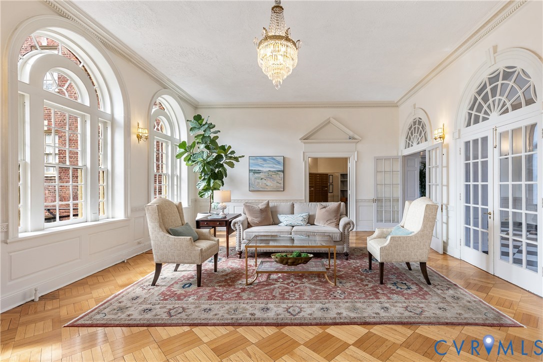 Parquet wood-finish flooring, arched windows with multi-pane detailing, crown molding, crystal chandelier, and paneled glass double doors