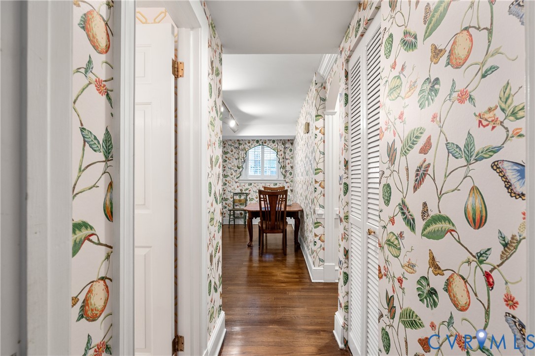 Hallway featuring botanical-patterned wallpaper, wood-finish flooring, and white louvered doors