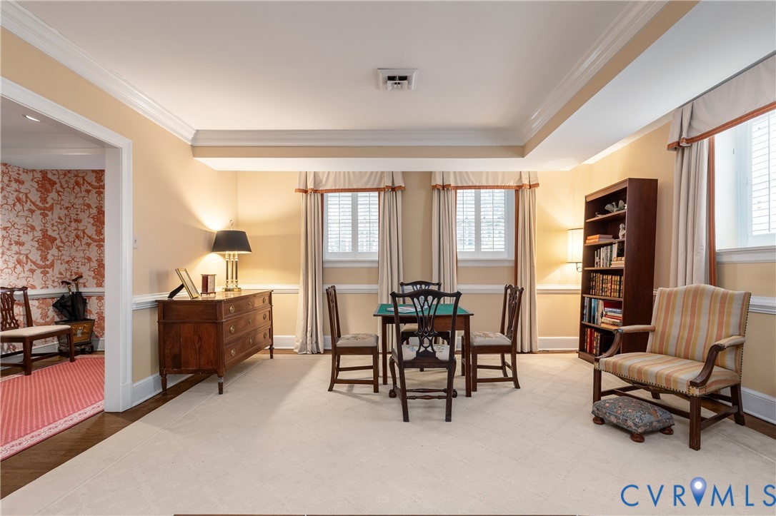 Room featuring crown molding, chair rail detailing, recessed ceiling tray, and dual windows with plantation shutters