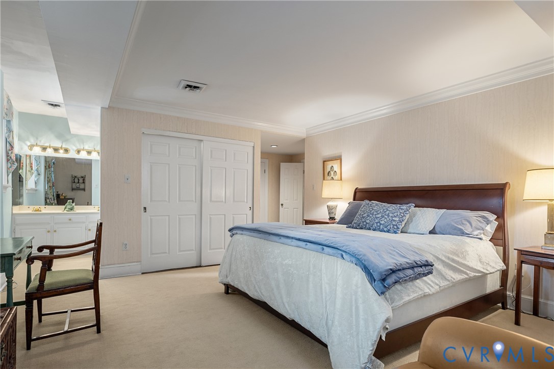 Neutral-toned wall covering, crown molding, double-door closet with recessed panels, and wall-to-wall carpeting