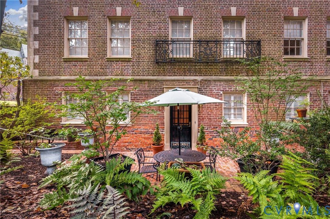 Brick exterior featuring a wrought iron balcony, multi-pane windows, and a brick patio
