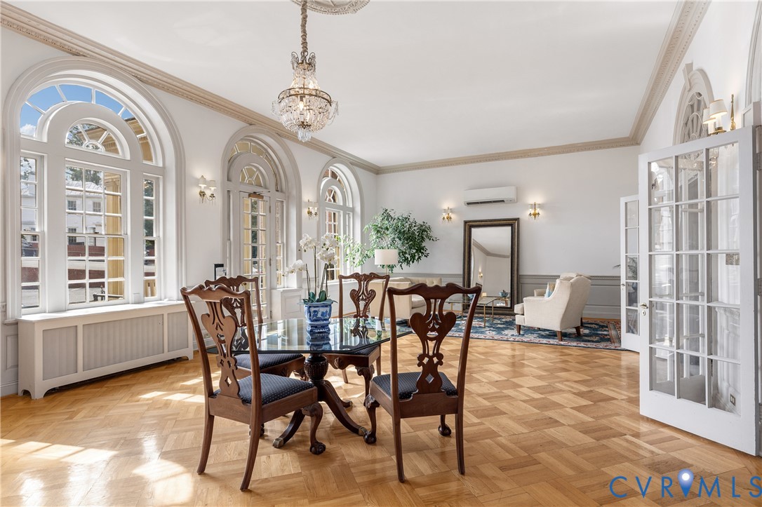 Parquet wood flooring, arched floor-to-ceiling windows, elaborate crown molding, crystal chandelier, and paneled glass doors
