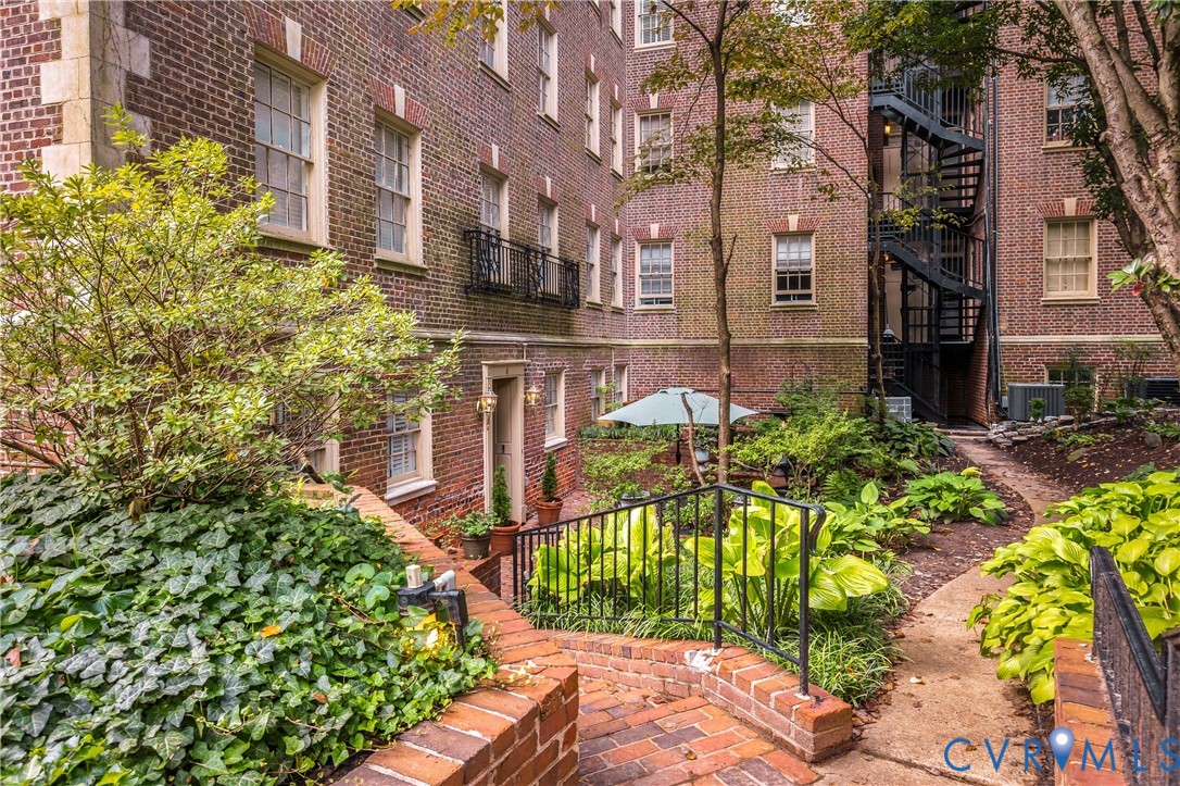 Classic brick exterior featuring a multi-story layout, wrought iron fire escape, decorative masonry detailing, a stone-paved walkway, and landscaped garden beds
