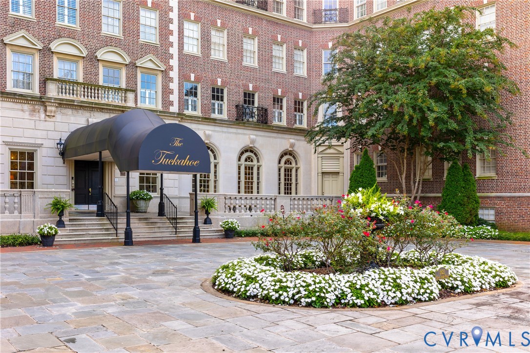 Classic brick exterior featuring a covered entryway with a decorative canopy, stone-paved motor court, stone balustrades, and a central landscaped garden bed