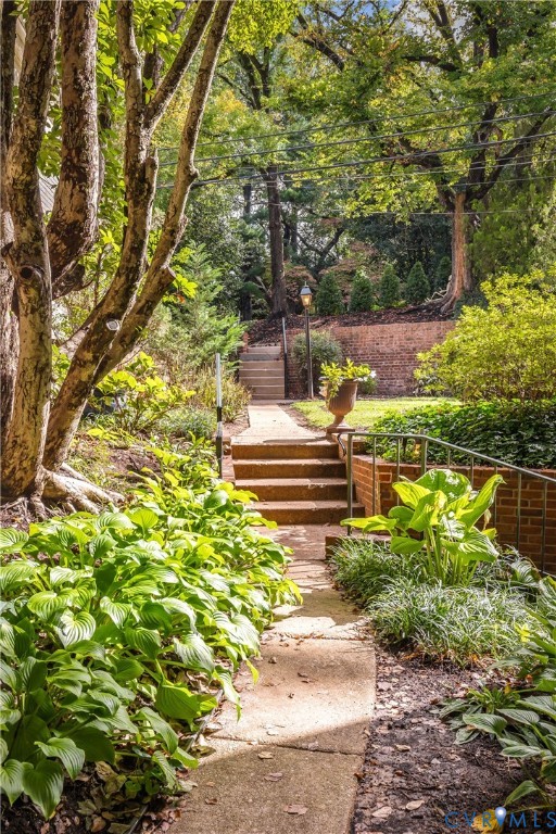 Landscaped garden path featuring brick retaining walls, concrete stairs with metal railings, mature trees, and perennial plantings