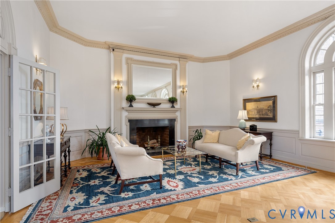 Parquet wood-finish flooring, fireplace with classic millwork mantel, arched windows, intricate ceiling crown molding, and paneled wainscoting