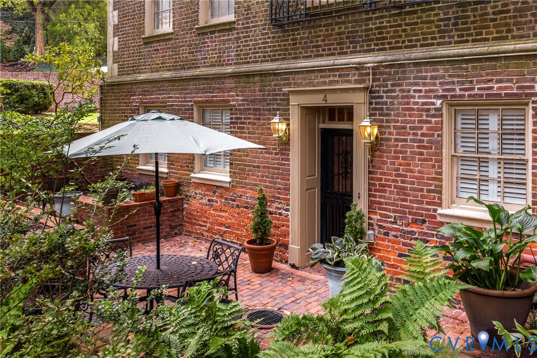Classic brick exterior featuring a multi-pane entry door with metal screen, multi-light windows with louvered shutters, traditional wall-mounted carriage lanterns, and a herringbone-patterned brick patio