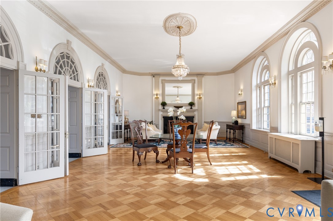 Parquet hardwood flooring, arched windows with fanlight transoms, crown molding with ceiling medallions, multi-pane glass French doors, and a decorative fireplace mantel