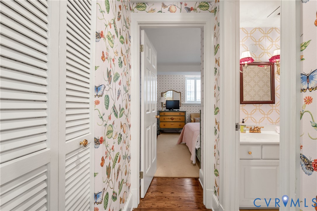 Hallway featuring wood-finish flooring, white louvered closet doors, and patterned wall coverings