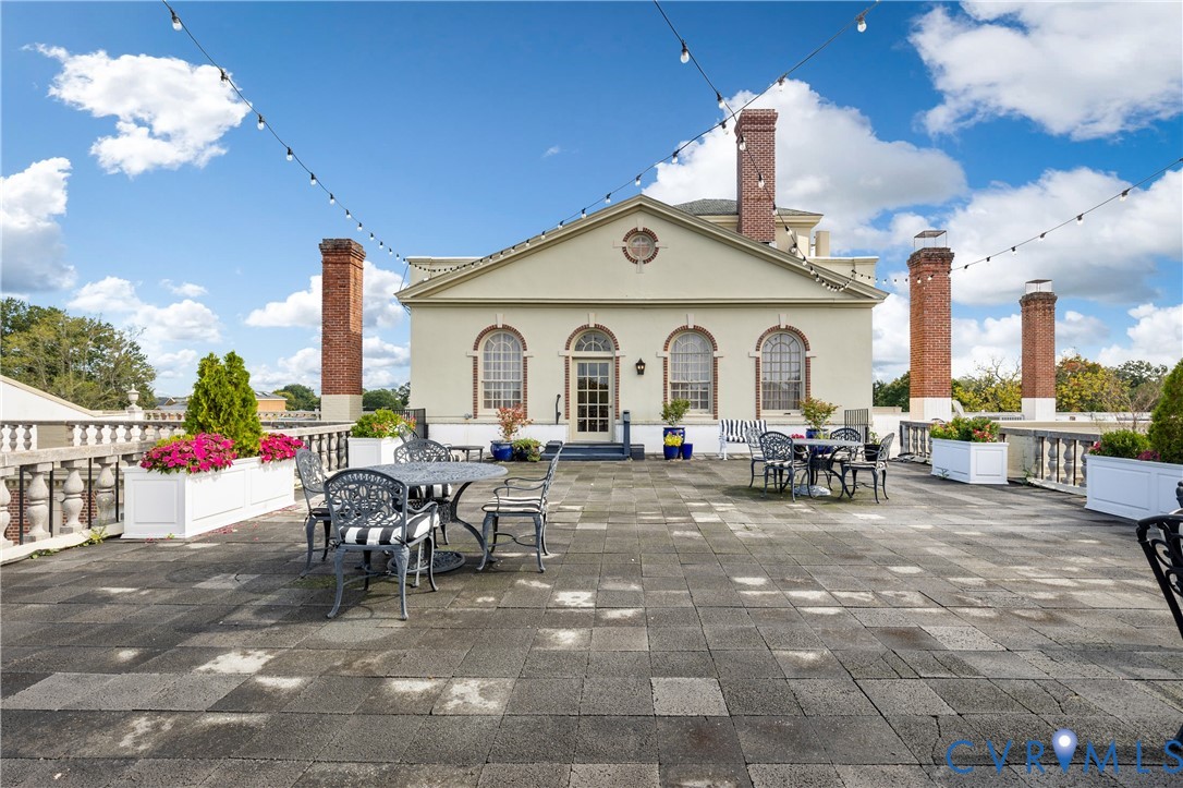 Rooftop terrace featuring concrete paver flooring, stone balustrade perimeter, integrated brick chimneys, and arched window details