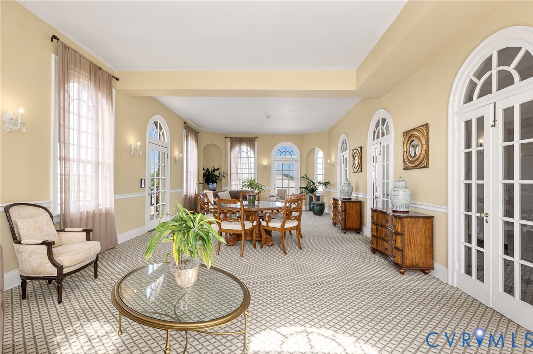 Expansive room featuring multi-pane arched windows, French door access, integrated wall niches, crown molding, and wall-mounted light fixtures