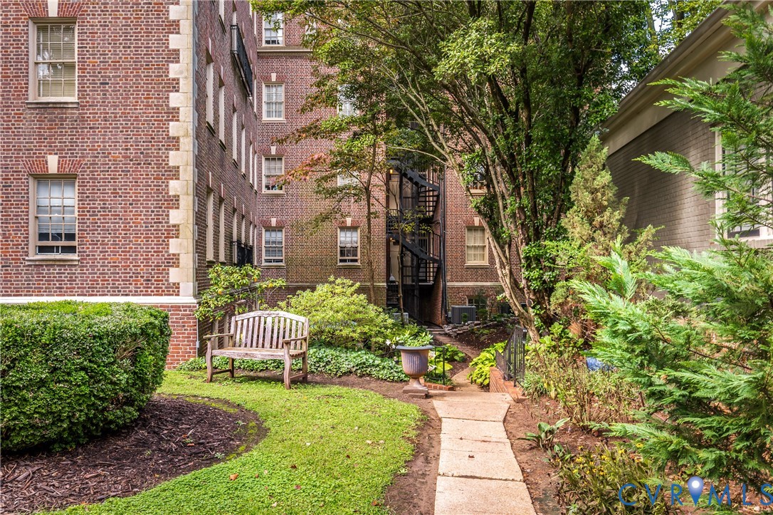 Classic red brick facade with stone quoins, manicured lawn, flagstone pathway, mature landscaping, and an iron spiral staircase