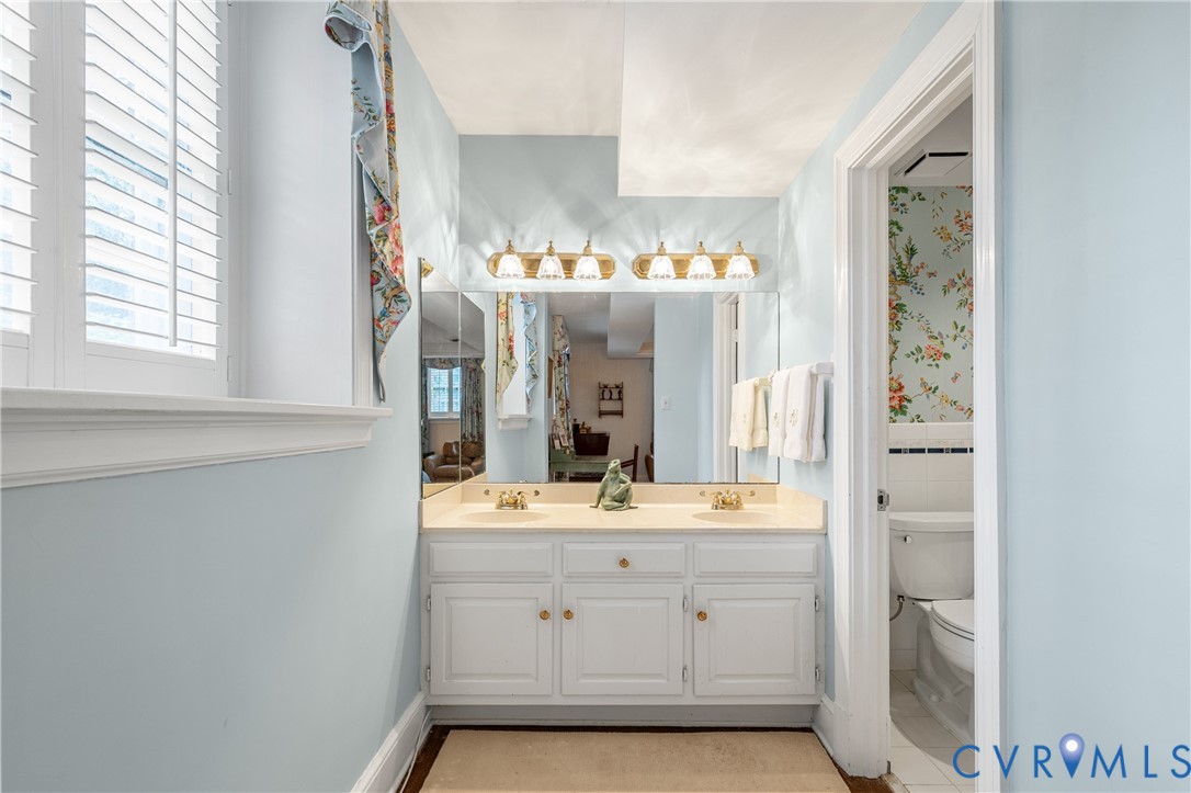 Double vanity featuring white cabinetry, a solid surface countertop with integrated dual sinks, a full-width vanity mirror, and multi-bulb wall-mounted lighting