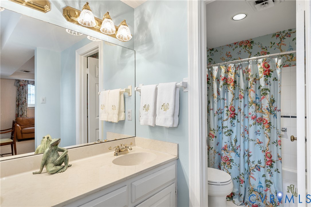 Full-width wall mirror, vanity with integrated basin, brass-finish lighting fixture, and white cabinetry