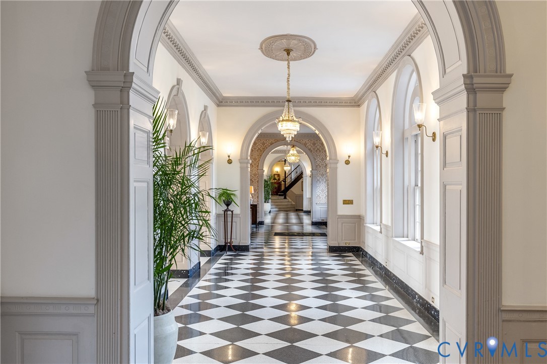 Grand hallway featuring arched entryways, checkerboard tile flooring, detailed crown molding, wainscoting, and crystal chandeliers