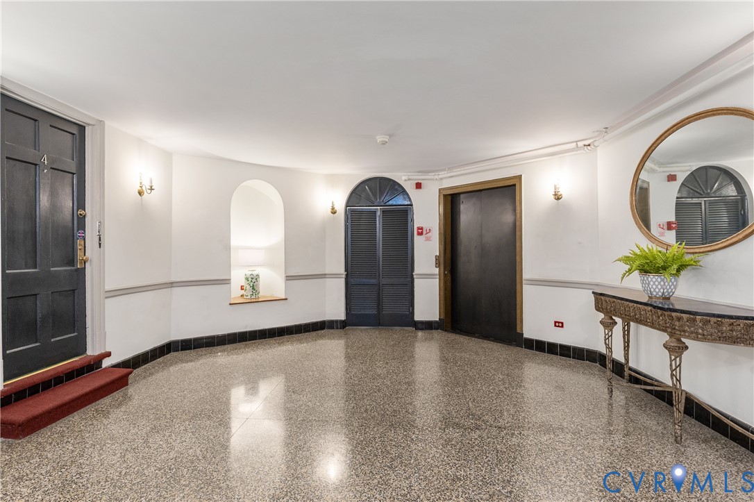 Polished terrazzo flooring, recessed wall niche, arched doorway with glass transom, high-gloss paneled doors, and crown molding detail