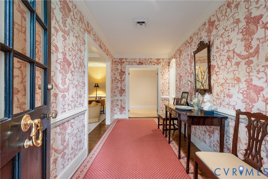 Foyer featuring patterned wall coverings, wainscoting, crown molding, wood-finish flooring, and a multi-pane glass-inlay door with polished brass hardware