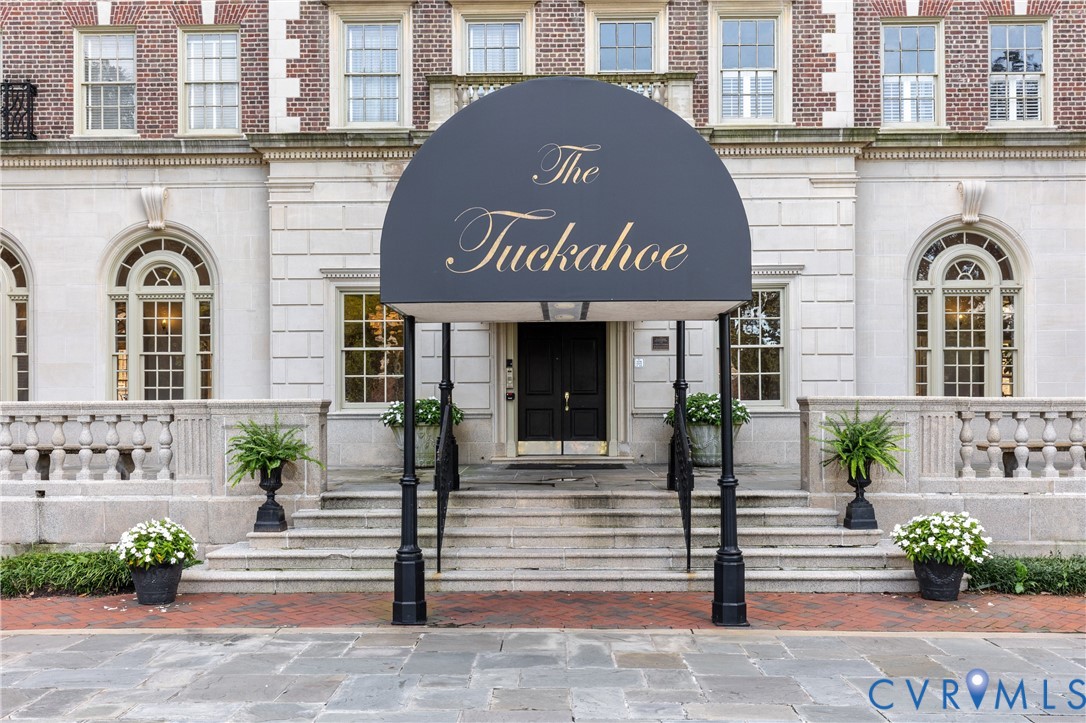 Classical stone facade featuring arched window casings, decorative balustrade railings, multi-pane windows, and a covered entryway with a metal canopy