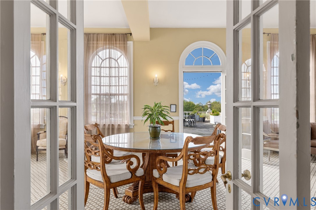 Sunroom featuring arched windows, tile flooring with a geometric pattern, wall-mounted sconce lighting, and an arched glass-paned door opening to an exterior terrace