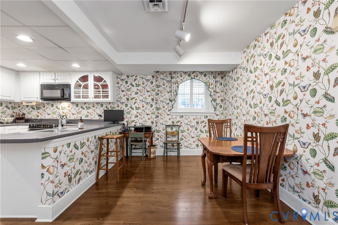 Kitchen featuring wood-finish flooring, white cabinetry, dark solid-surface countertops, built-in microwave, and arched window with interior shutters