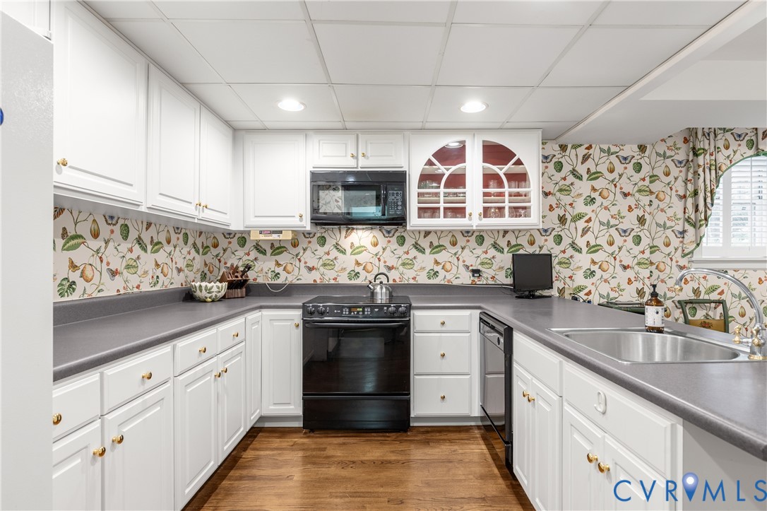 Kitchen featuring white shaker-style cabinetry, solid-surface countertops, built-in glass-front upper cabinets, stainless steel sink, and wood-finish flooring