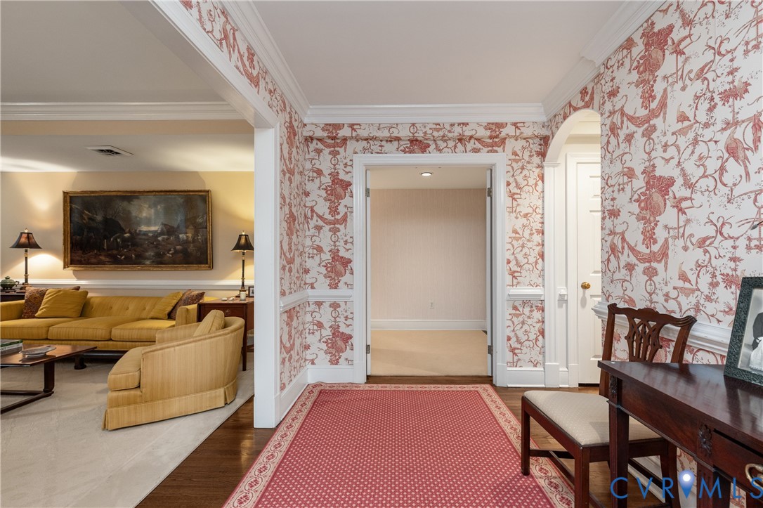 Foyer featuring patterned wall coverings, chair rail molding, crown molding, arched entryways, and wood-finish flooring
