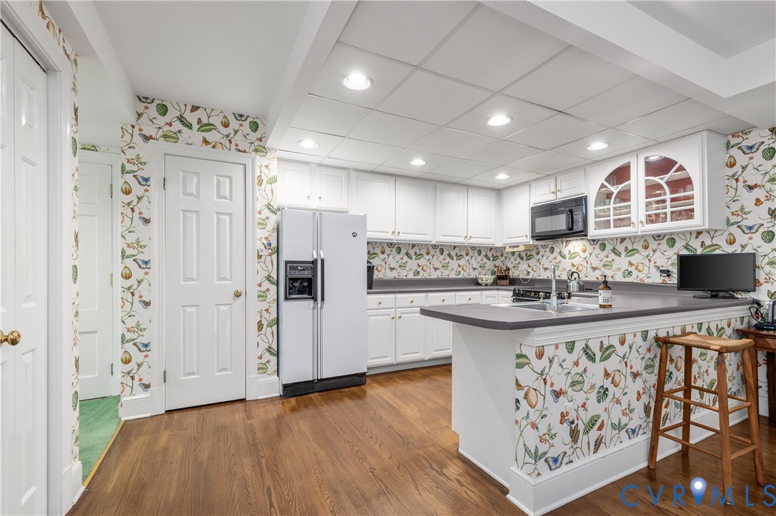 Kitchen featuring white cabinetry, solid-surface countertops, wood-finish flooring, recessed lighting, and upper cabinets with glass-paneled doors
