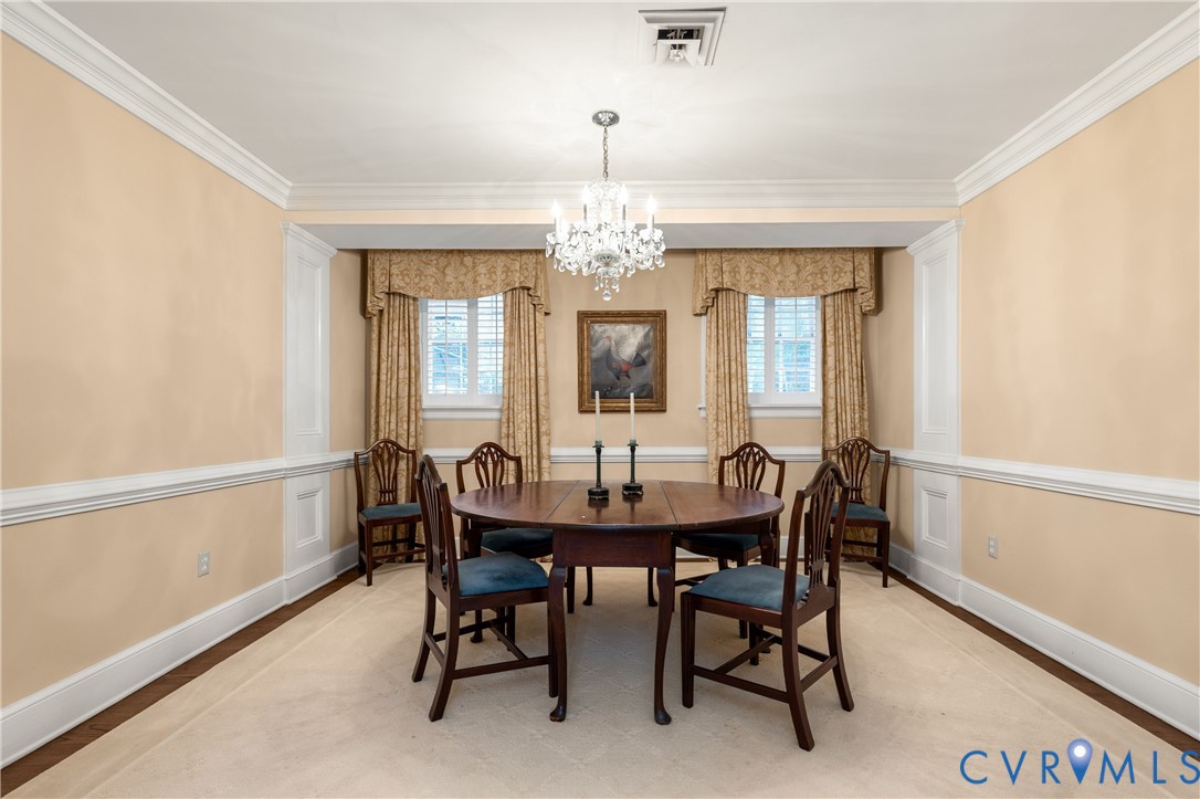 Formal dining area featuring decorative wall wainscoting, crown molding, multi-pane windows with interior shutters, and a central crystal chandelier